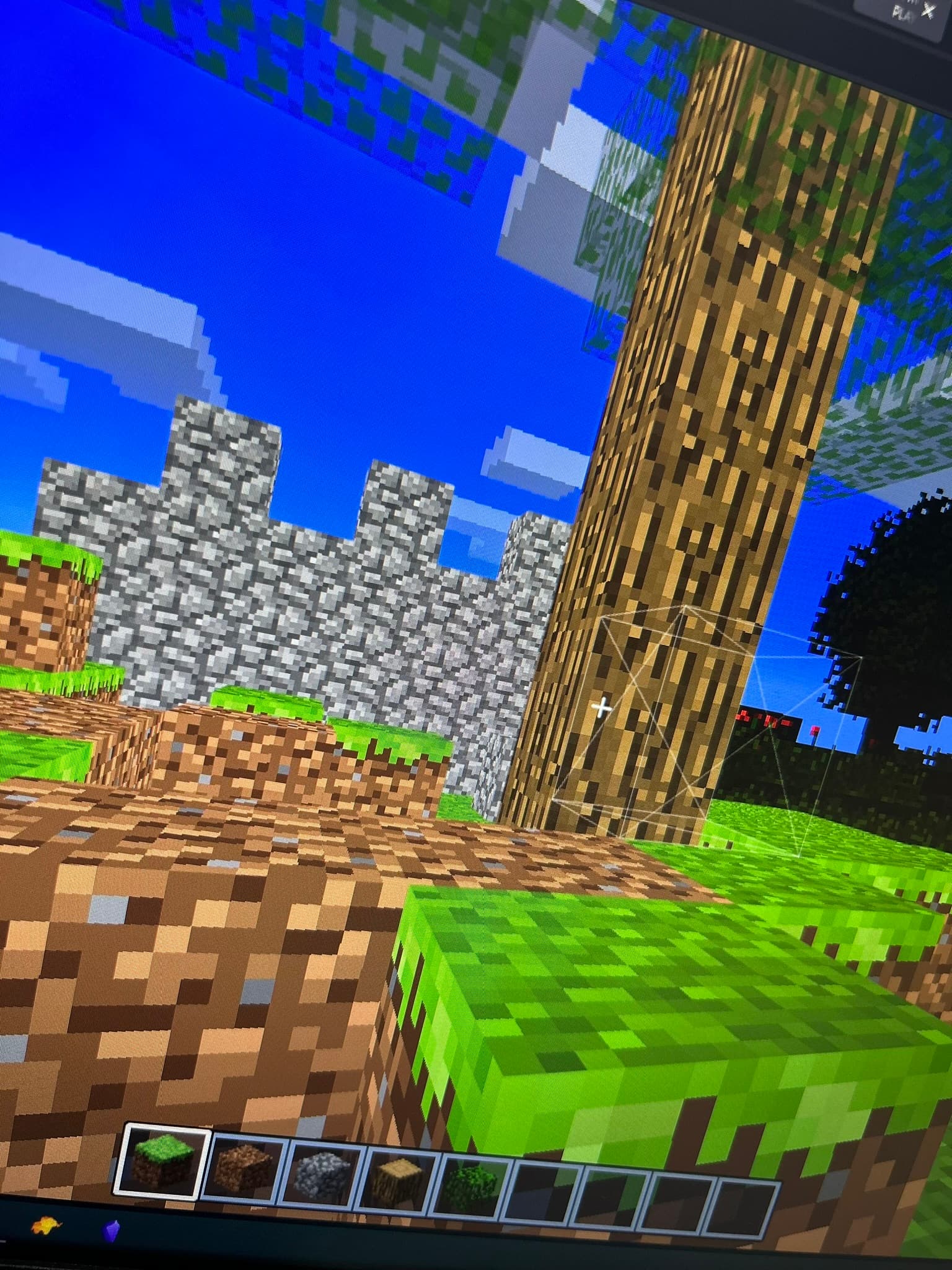 A Minecraft-like sandbox game. There's a block selector at the bottom which includes a grass, dirt, cobblestone, wood and leaves block. In front, there are grass and leaves block placed in the terrain.